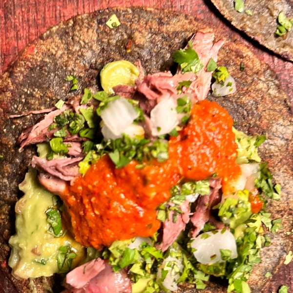 Close-up of a Taza Modern Mexican taco with meat, guacamole, salsa, onions, and cilantro.